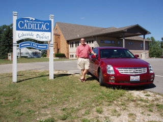 Scott showing his new 2005 Cadillac STS next to the welcome to Cadillac Michigan sign